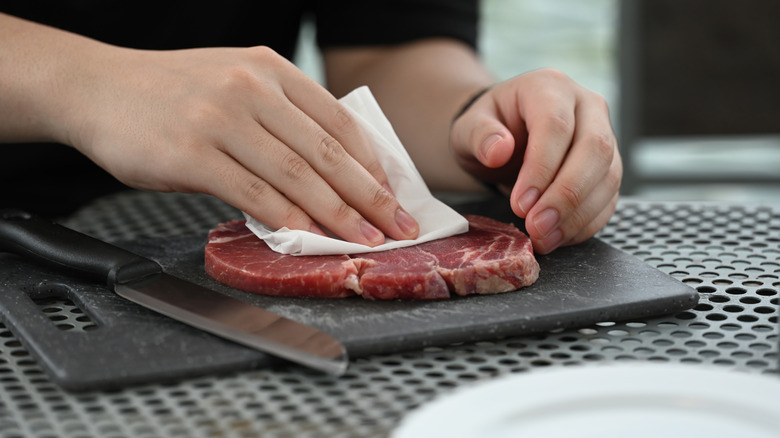 Hands patting steak dry on black cutting board