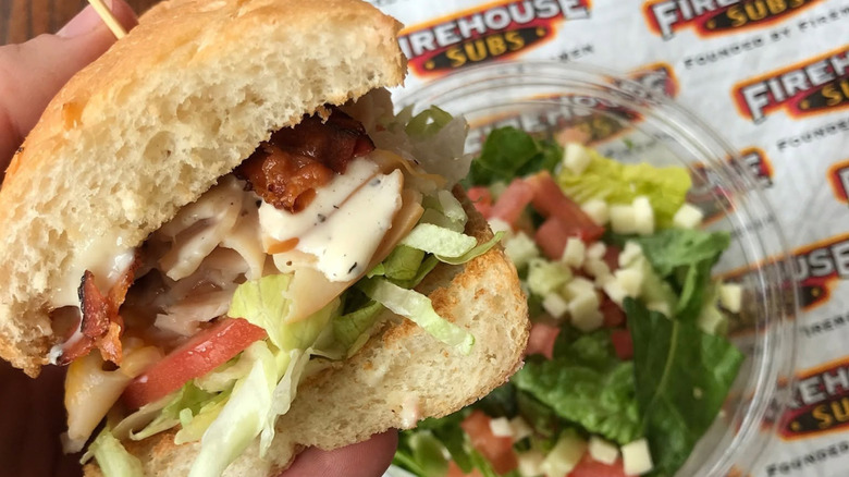 Sandwich being held above a side salad on a branded paper from Firehouse Sub