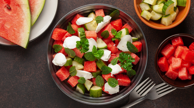 Salad of cubed watermelon, cucumber, mint leaves, and burrata cheese in silver bowl