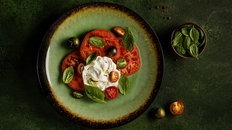 Green plate with stracciatella cheese, tomato slices, and basil leaves