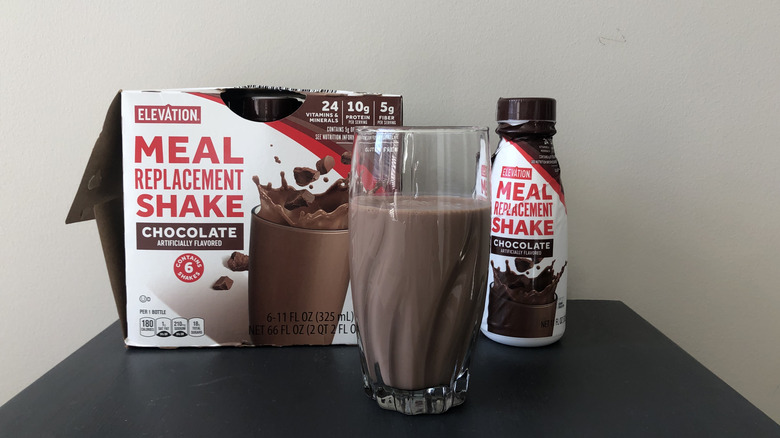Bottles of Aldi Elevation chocolate meal replacement shake with some poured into a glass