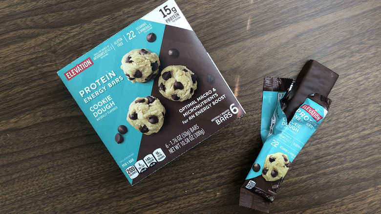 A box of Aldi Elevation cookie dough protein energy bars with an open bar beside it