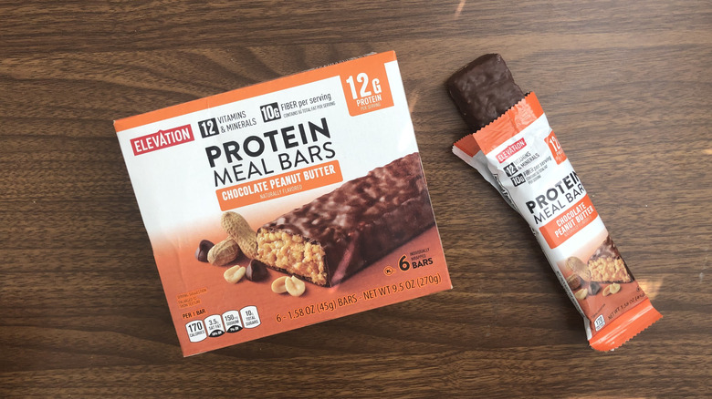 A box of Aldi Elevation chocolate peanut butter protein meal bars with one bar open next to it