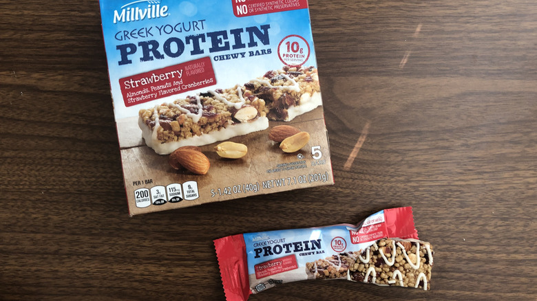A box of Aldi Millville strawberry Greek yogurt protein chewy bars and one open bar beside it