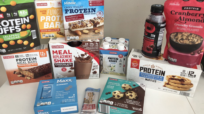 12 protein snacks and drinks from Aldi in the packaging stacked on a white table