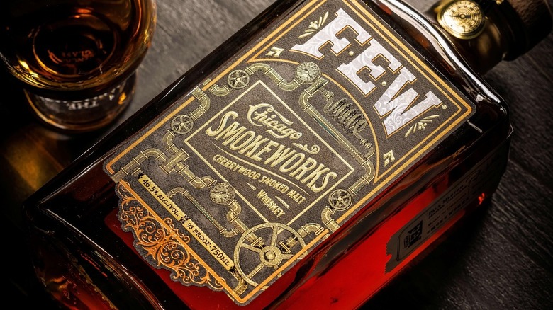 A close up of a bottle of FEW Chicago Smokeworks laid on a table next to a filled glass