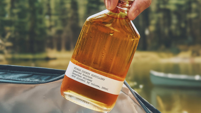 A person pulling a small bottle of Kings County Distillery Peated Bourbon from a bag outdoors
