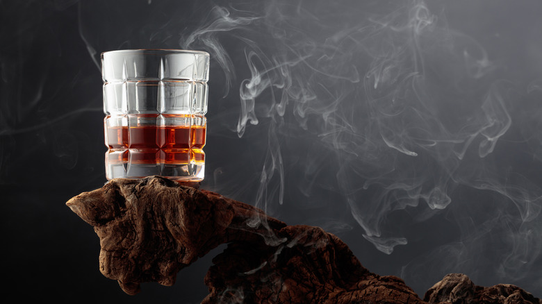 A glass of whiskey posed on a stylized wooden platform surrounded by wispy smoke