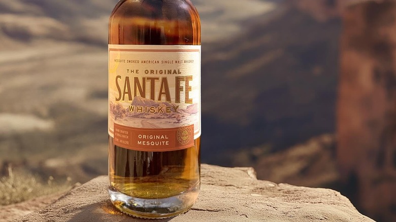 A bottle of Santa Fe Original Mesquite posed outdoors in a blurred rocky landscape