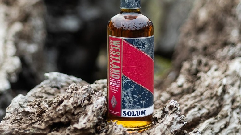 A bottle of Westland Solum posed on a rocky outdoor setting with a blurred background