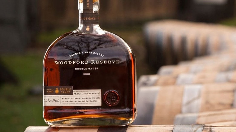 A bottle of Woodford Reserve Double Oaked posed on the edge of a whiskey barrel