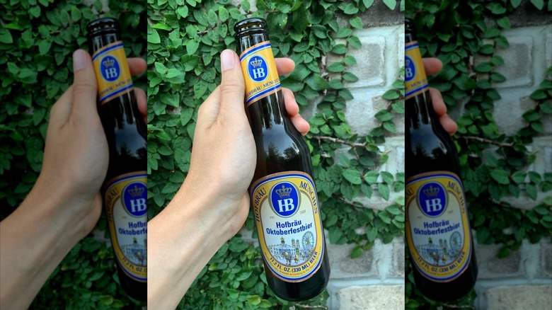 Hand holding bottle of Hofbrӓu Oktoberfestbier in front of wall and greenery