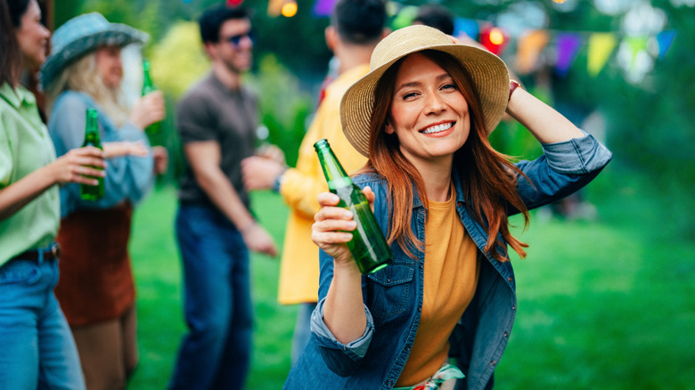 Smiling woman with bottle of beer outside and friends blurred in background