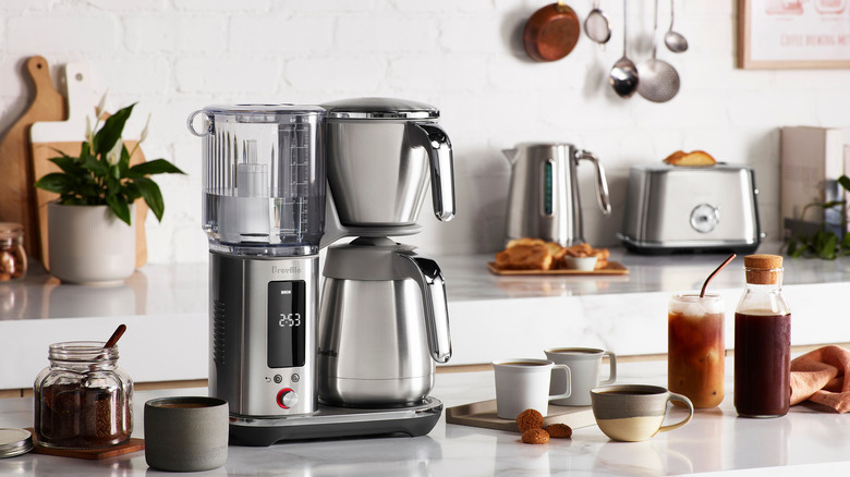 A Breville coffee maker on a kitchen island surrounded by cups of coffee