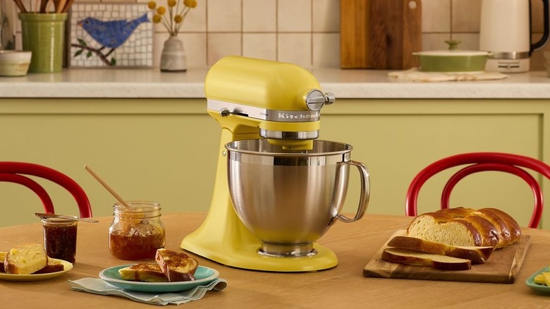 A butter yellow KitchenAid stand mixer on a kitchen table surrounded by breakfast items