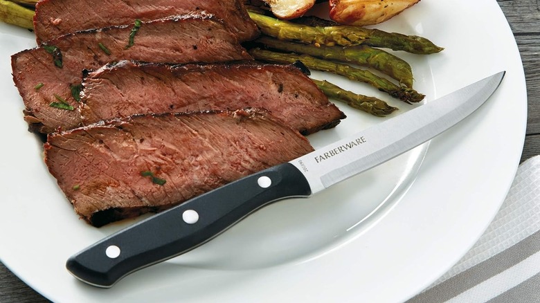 A Farberware steak knife shown on a plate of food that includes steak.