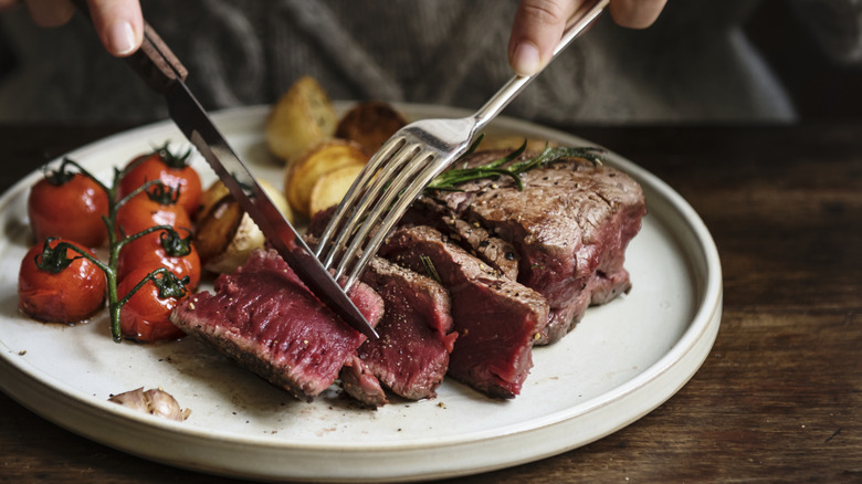 A person cutting steak on a plate with a steak knife
