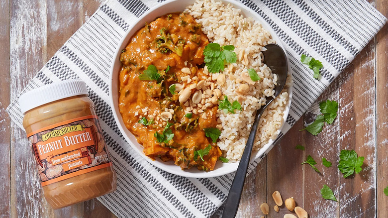 Jar of peanut butter placed alongside bowl of rice and peanut curry