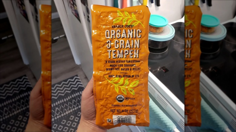 Hand holding unopened package of Trader Joe's tempeh in kitchen
