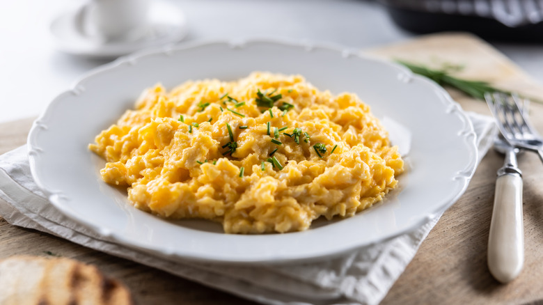 Scrambled eggs on white plate, garnished with chopped chives