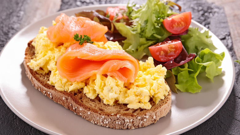 Plate of scrambled eggs and smoked salmon on toast with side salad