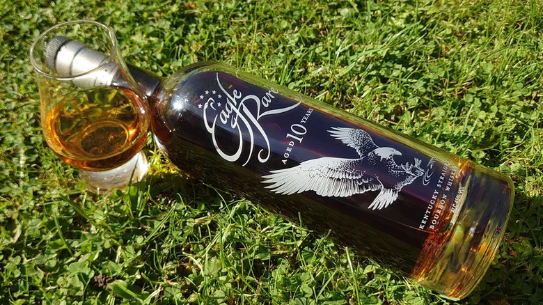 A bottle of Eagle Rare 10-Year laid on its side on grass next to a filled glass