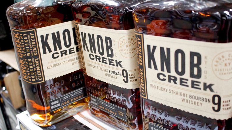 A row of Knob Creek 9-Year bottles on a liquor shelf with one turned to its side