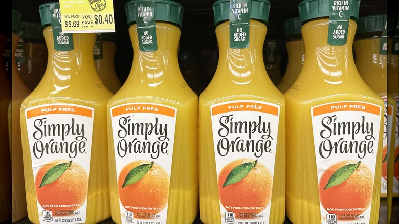 Four yellow bottles of Simply Orange juice in a store.