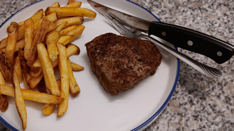 LongHorn filet mignon with French fries on white plate with blue trim and silverware