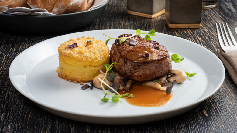 filet mignon with sauce and sides on white plate on wooden table