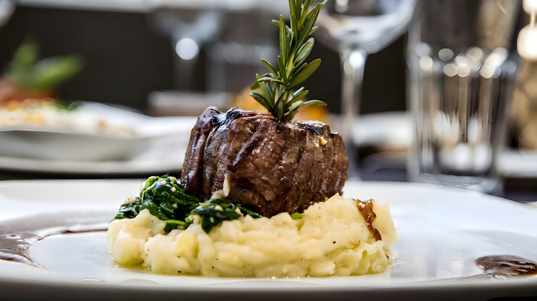 Cooked filet mignon on bed of mashed potatoes topped with herbs