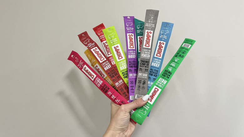 Hand holding different Chomps meat stick flavors.