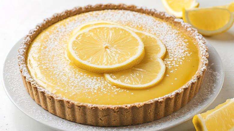 A whole lemon tart topped with lemon slices and powdered sugar
