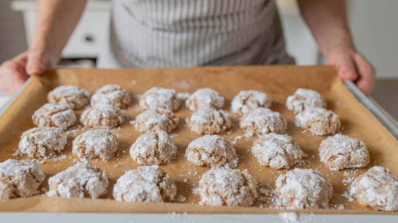 A person holding a baking tray of amaretti biscuits