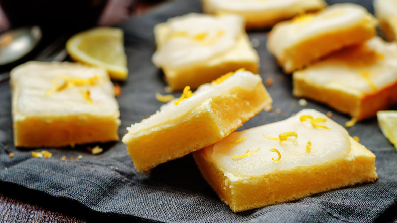 Several lemon bars with icing served on a dark napkin