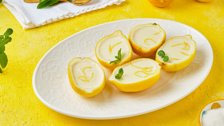 Lemon posset, served in lemon skins on a white plate, placed on a yellow surface