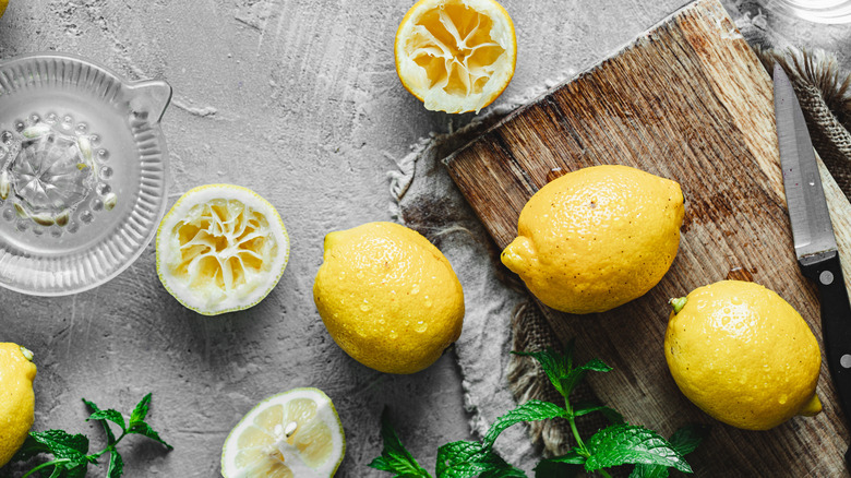 A bunch of whole and cut lemons with a cutting board and juicer