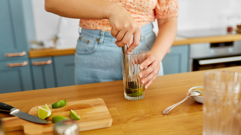 person muddling lime and mint in glass