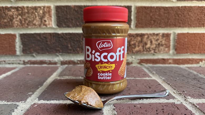 Jar of Lotus Biscoff crunchy cookie butter behind spoonful of thick cookie butter on brick surface