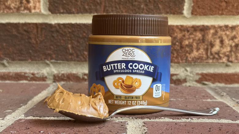 Jar of ChocZero butter cookie speculoos spread behind spoonful of creamy cookie butter on brick surface
