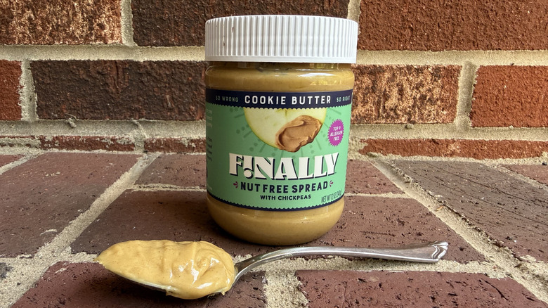 Jar of Finally cookie butter nut free spread behind spoonful of drippy cookie butter on brick surface