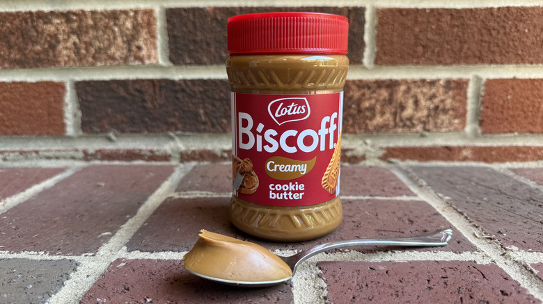 Jar of Lotus Biscoff creamy cookie butter behind spoonful of smooth cookie butter on brick surface