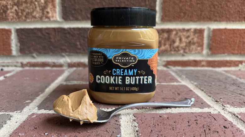 Jar of Private Selection creamy cookie butter behind spoonful of thick cookie butter on brick surface