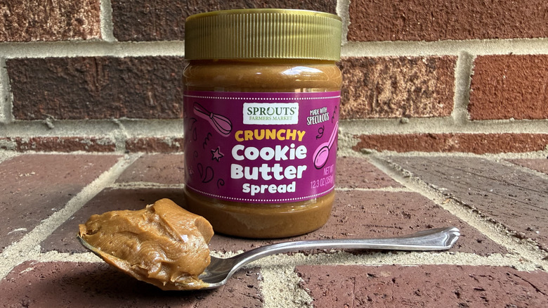 Jar of Sprouts crunchy cookie butter spread behind spoonful of thick cookie butter on brick surface