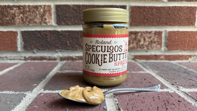 Jar of Roland crunchy cookie butter spread behind spoonful of drippy cookie butter on brick surface