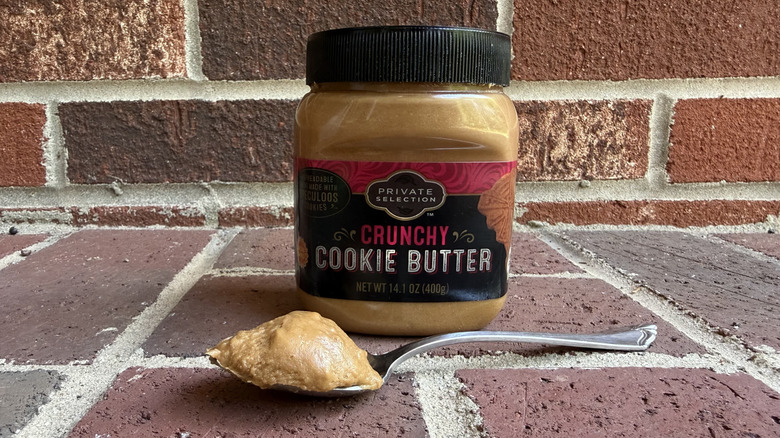 Jar of Private Selection crunchy cookie butter behind spoonful of thick cookie butter on brick surface