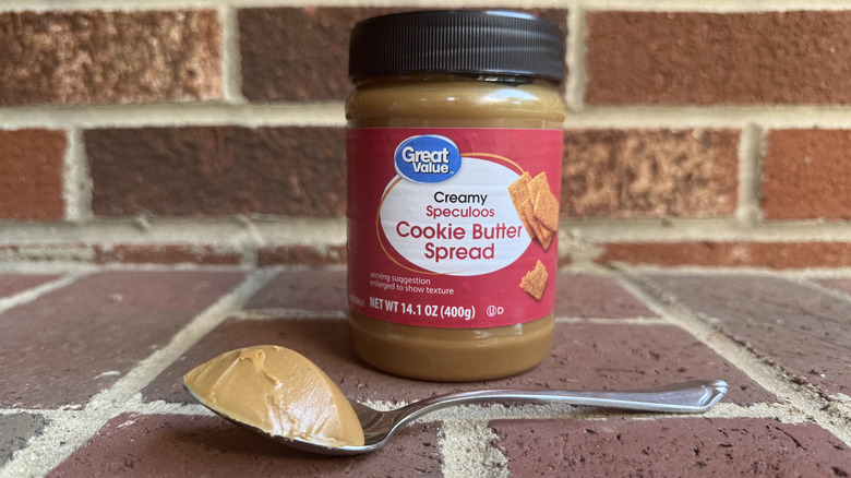 Jar of Great Value creamy speculoos cookie butter spread behind spoonful of creamy cookie butter on brick surface