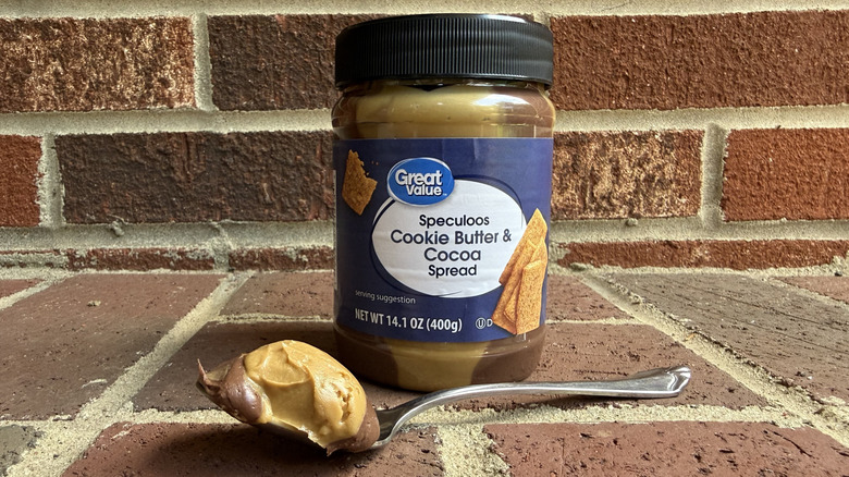 Jar of Great Value speculoos cookie butter and cocoa spread behind spoonful of creamy cookie butter on brick surface