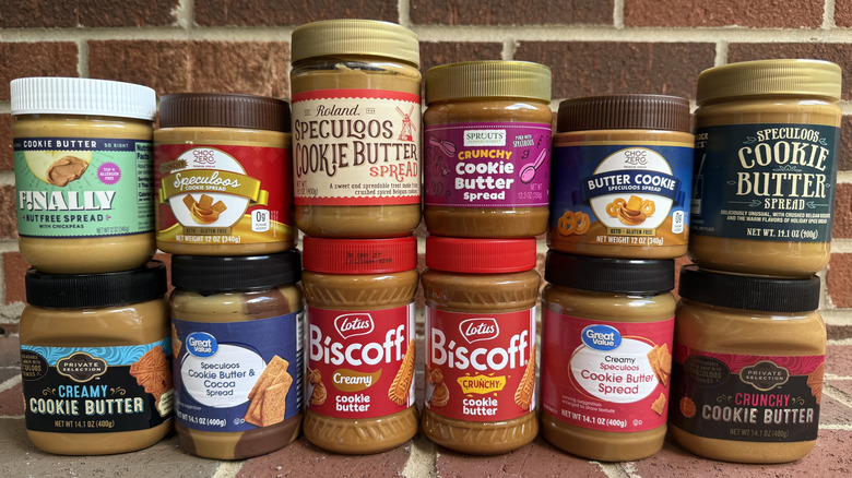 12 jars of cookie butter from different brands lined up on brick surface