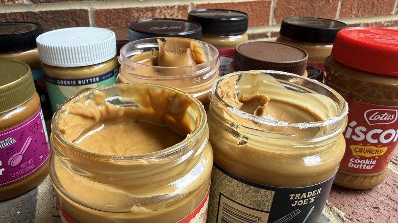 Close to a dozen cookie butter jars on brick surface, with three open to show cookie butter inside